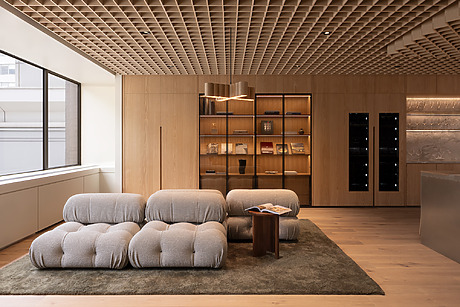 Modern office space with stylish beige tufted sofas, wooden shelves, and large windows allowing natural light.