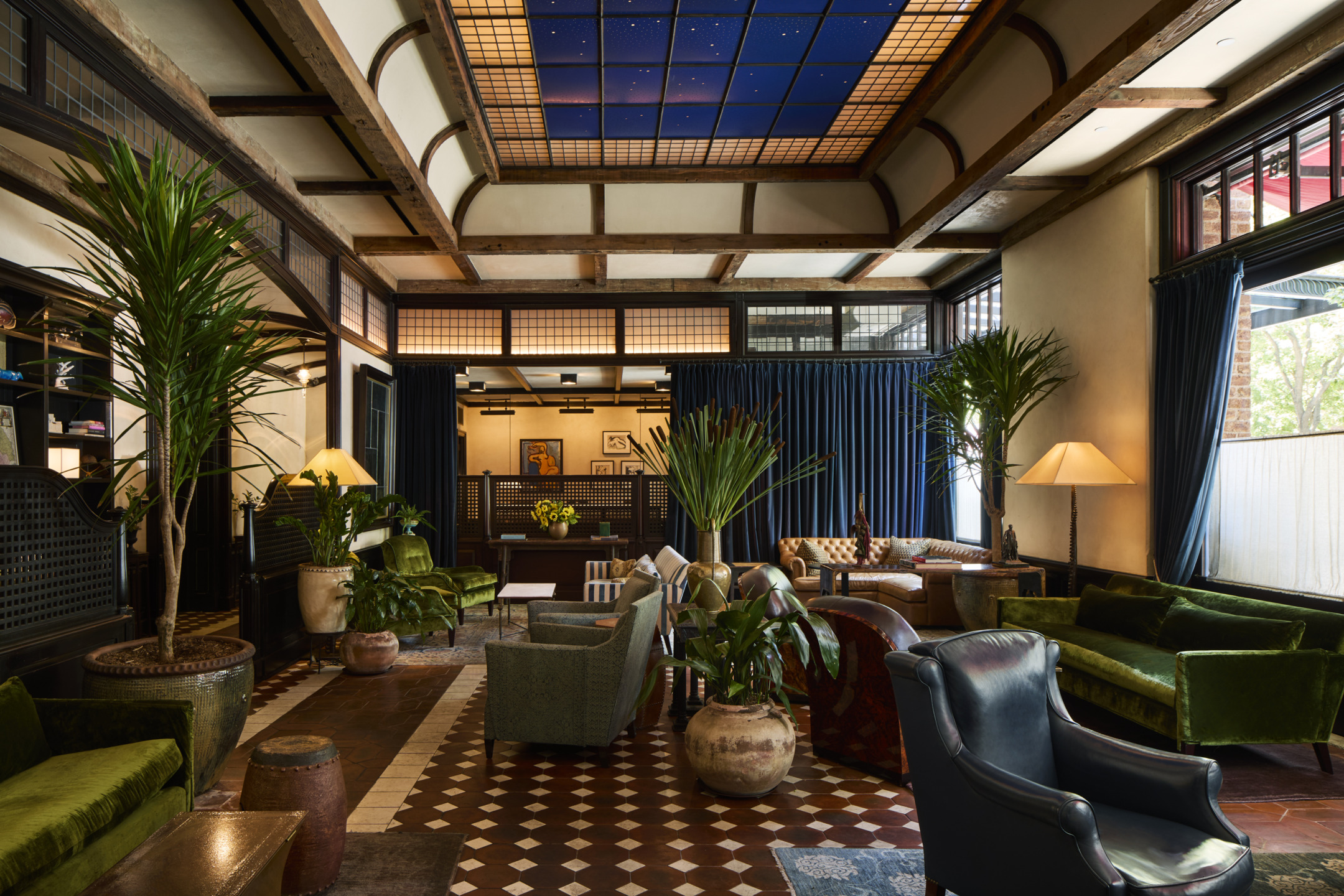 Cozy hotel lobby with green sofas, armchairs, large plants, and a ceiling with starry sky design.