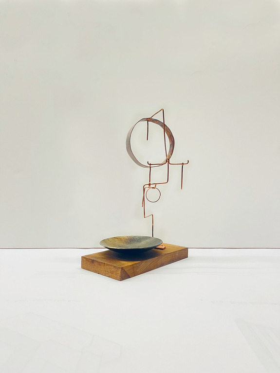 Abstract metal sculpture on a wooden base with circular shapes and geometric elements against a plain background.