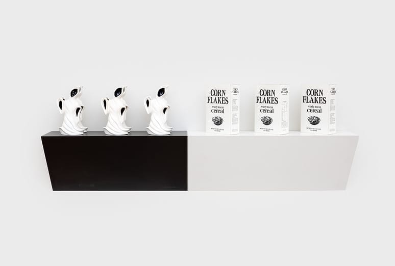 Modern art display with five sculpted figures and three boxes of corn flakes on a contrasting black and white shelf.