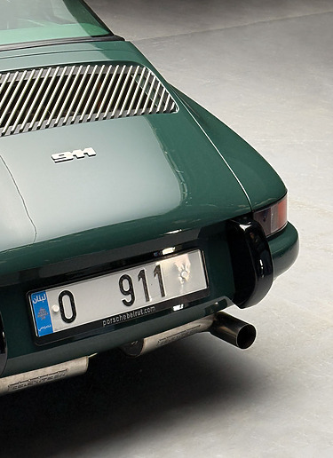 Rear view of a vintage green sports car with distinct taillights and chrome detailing.
