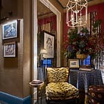 Elegant reading nook with patterned chair, framed art, and a table adorned with a vibrant floral arrangement and table lamp.