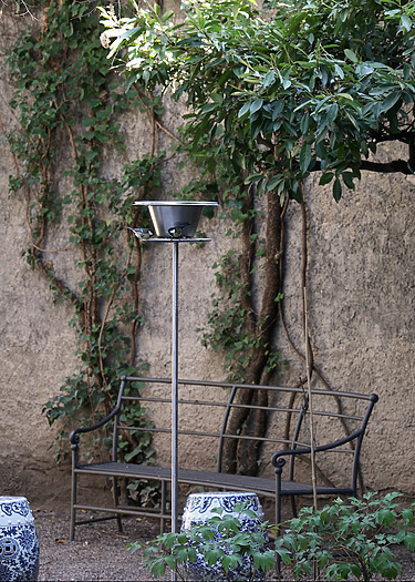 Garden setting with a metal bench and tall lamp surrounded by potted plants and ivy on a textured stone wall.