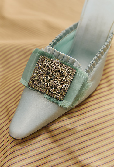 Elegant satin shoe with ornate metal buckle on a striped fabric background.