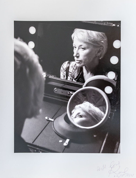 Woman looking in a mirror with lights in a black and white photograph.
