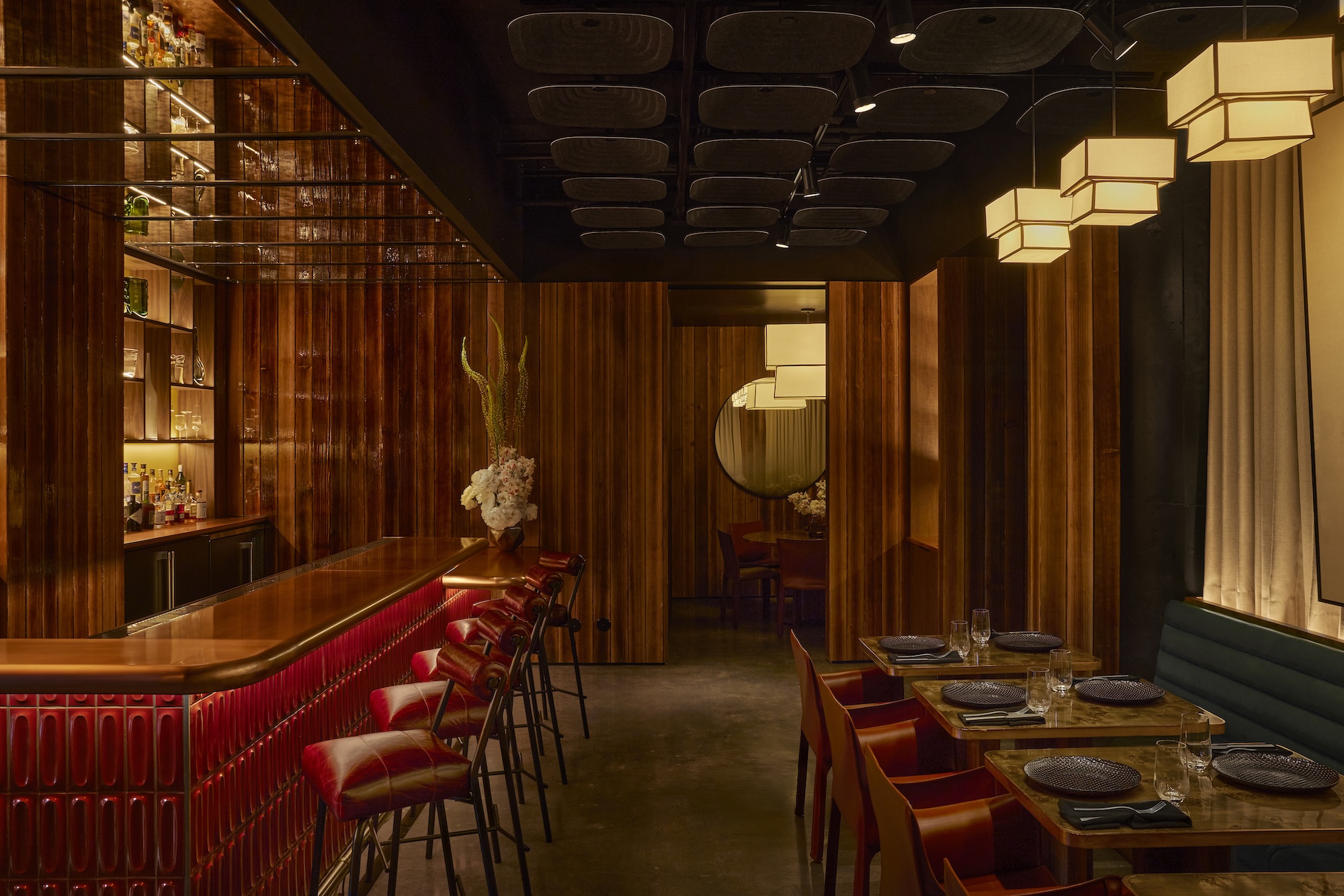Cozy restaurant interior with wooden walls, a bar with red seats, ambient lighting, and a set dining table.