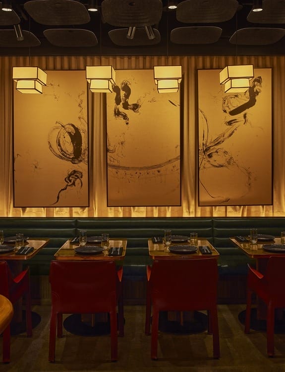 Dimly lit modern restaurant interior with abstract art on walls, red chairs, and set tables for dining ambiance.