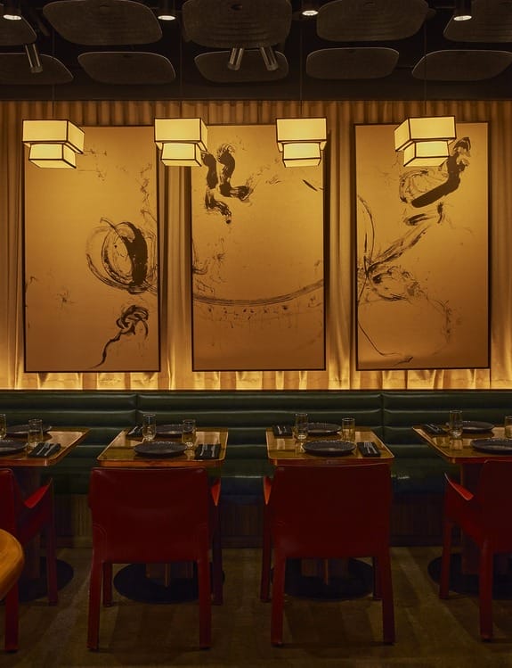 Dimly lit modern restaurant interior with abstract art on walls, red chairs, and set tables for dining ambiance.