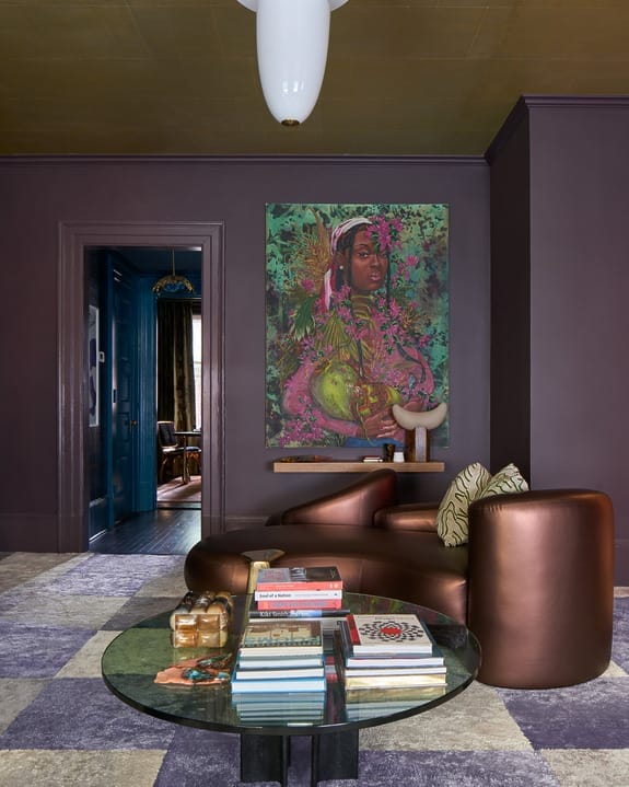 Modern living room with a large colorful portrait on wall, sleek brown armchairs, and a glass coffee table with books.