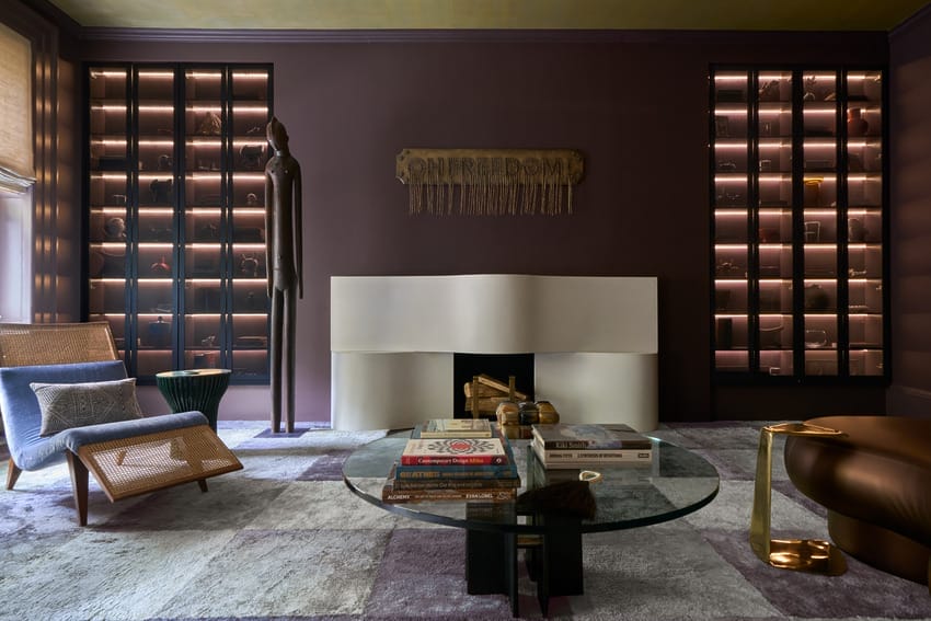 Cozy modern living room with purple walls, fireplace, glass coffee table, and decorative bookshelf display.