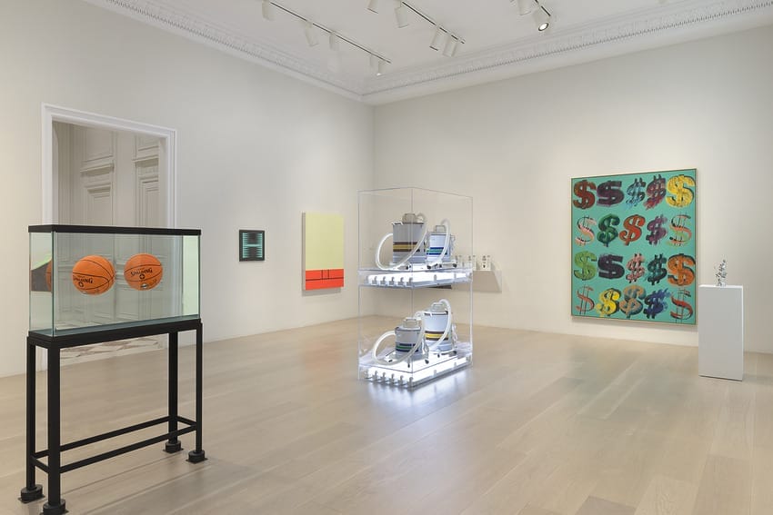 Contemporary art gallery with various colorful paintings and illuminated sculptures on display in a spacious room.