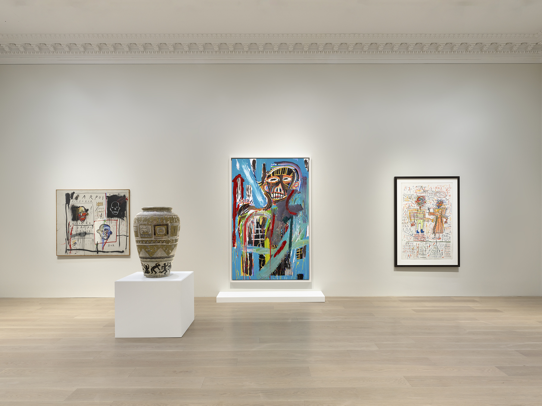 Art gallery exhibit featuring colorful paintings, intricate drawings, and a decorative vase on display in a minimalist setting.