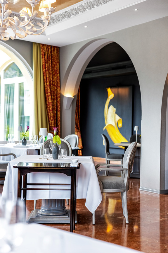 Elegant restaurant interior with arched doorways, contemporary artwork, and tables set for dining.