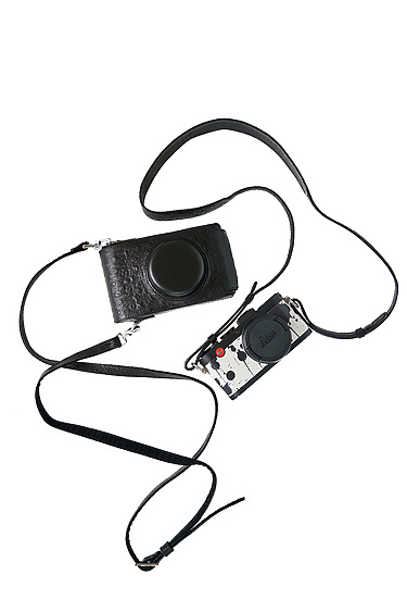 Stylish black and white camera with leather case and adjustable strap laid out on a white background.