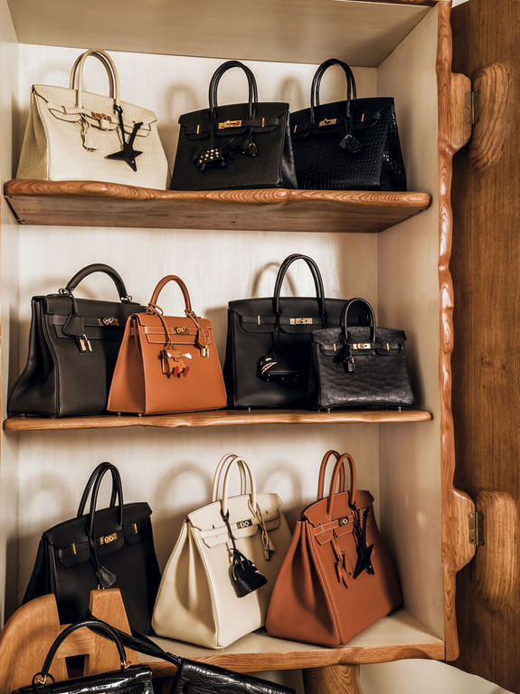 Collection of luxury handbags displayed on wooden shelves, featuring various styles and colors, in an elegant setting.