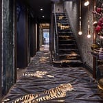 A luxurious hallway with tiger-patterned carpet running up the stairs and along the floor, adorned with hanging lights.