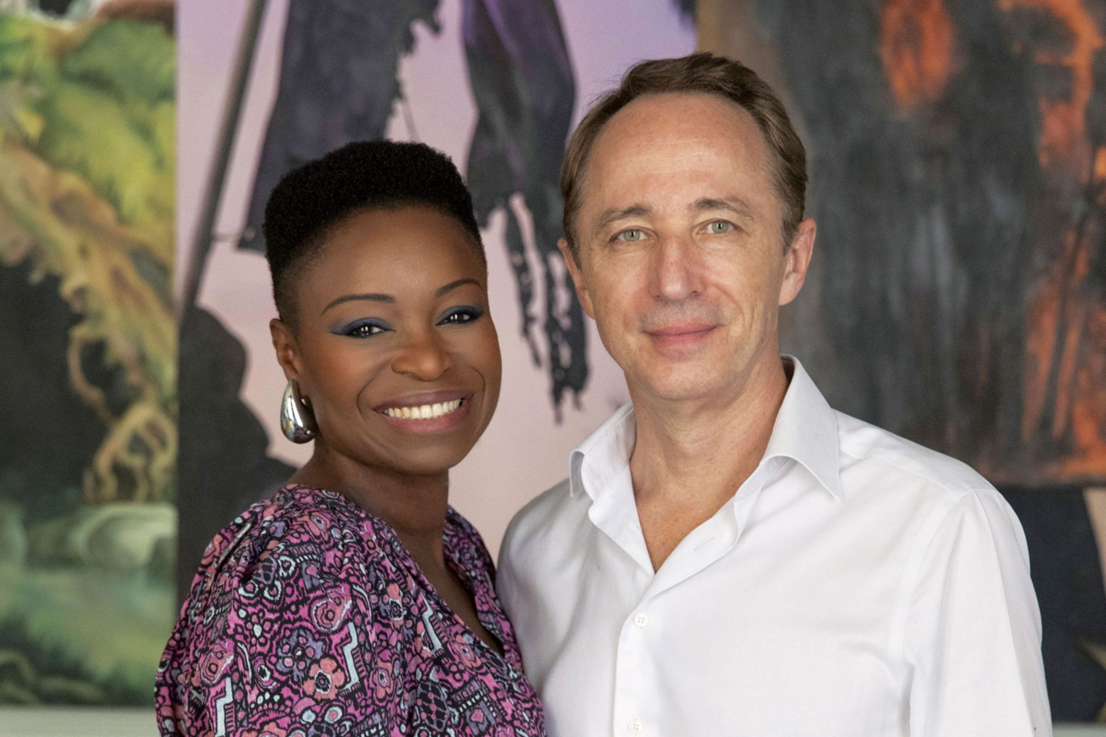 Two people smiling in front of abstract artwork background.