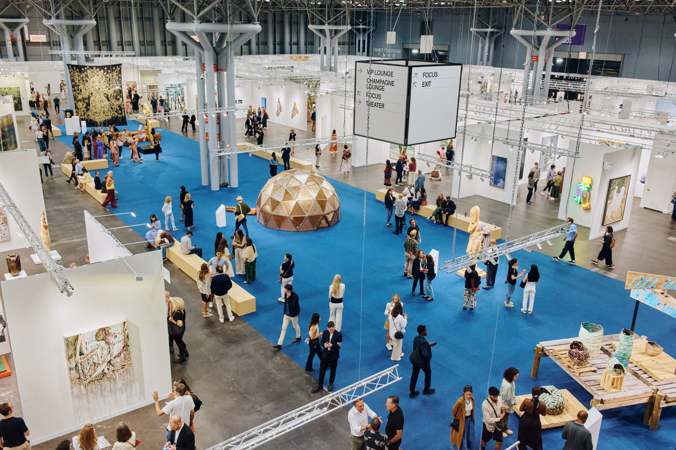 Aerial view of a bustling art exhibition with visitors exploring various artworks and installations in a spacious hall.