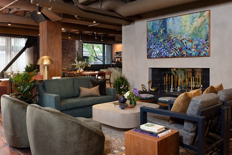 Modern living room with green sofa, armchairs, coffee table, colorful painting, plants, and decorative items near a fireplace.