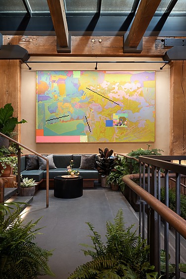 Colorful abstract painting in a modern room with plants, wooden beams, and cozy seating area.