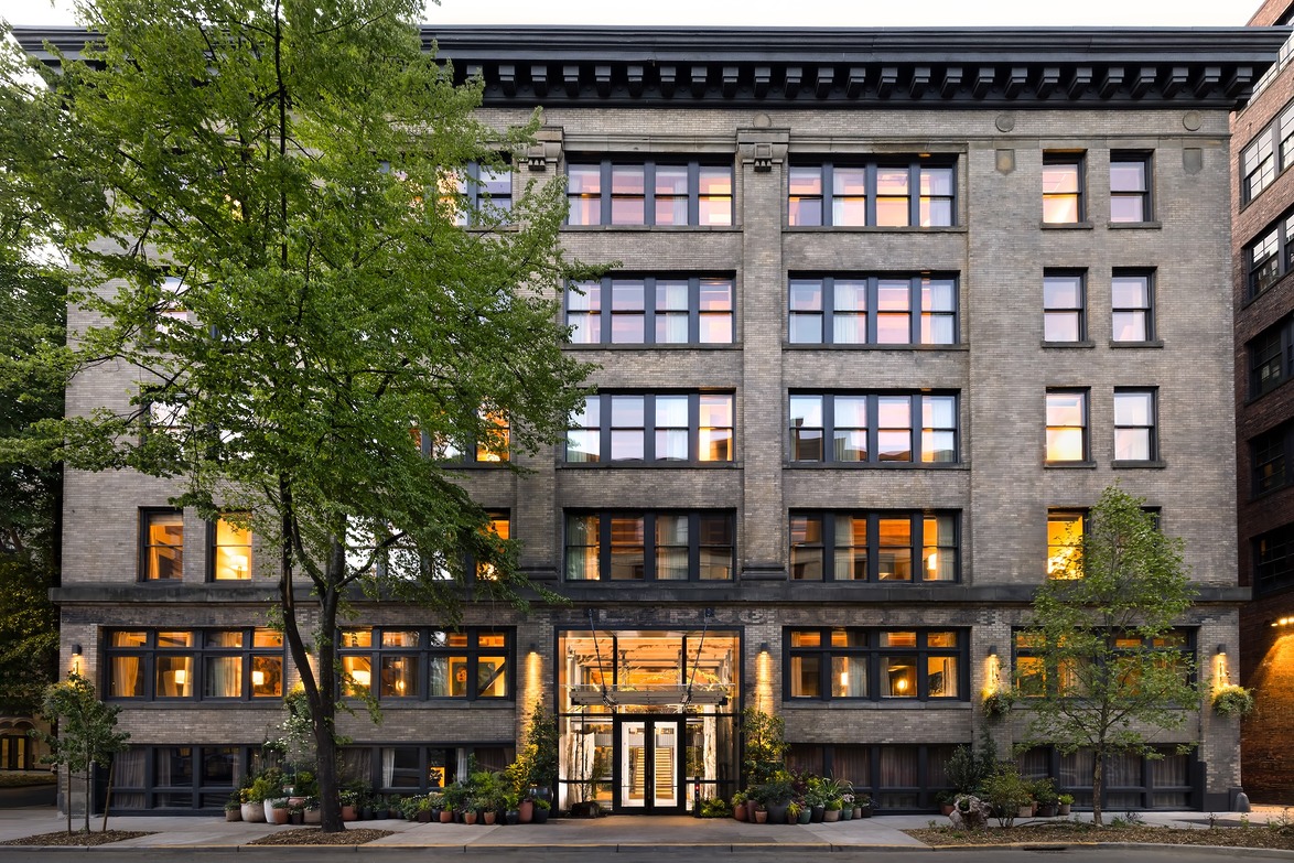 Front view of a stylish urban apartment building with illuminated windows and surrounding trees.
