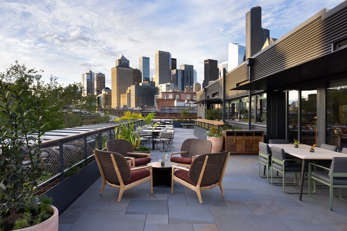 Rooftop patio with seating and plants overlooking a city skyline on a clear day