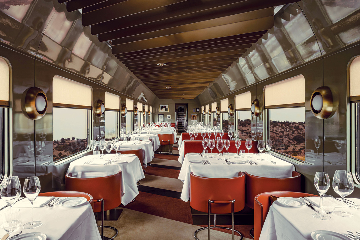Luxurious train dining car with elegantly set tables, ready for guests, panoramic windows offering scenic views of the landscape.