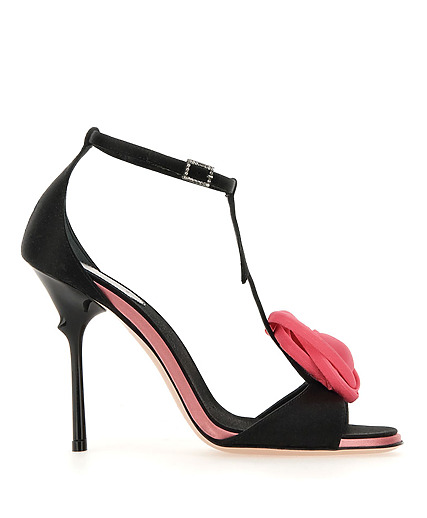 Black high-heeled sandal with pink rose decoration on the front strap and ankle buckle strap, side view.
