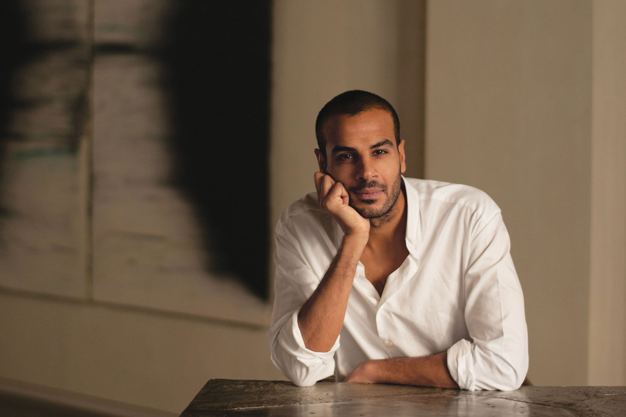 Man in a white shirt leaning on a table with an abstract painting in the background.