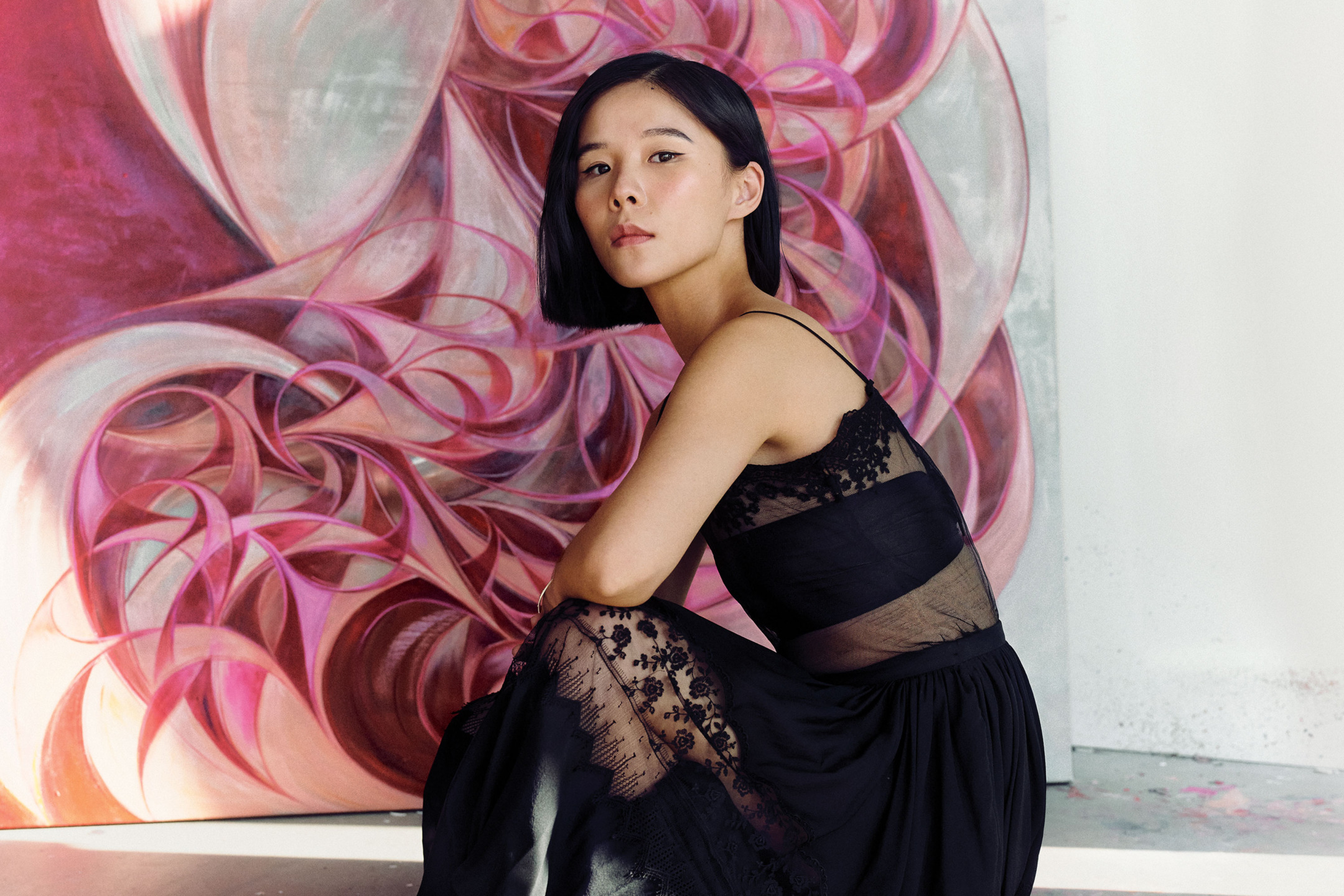 Woman in a black dress sitting in front of an abstract pink and red artwork.
