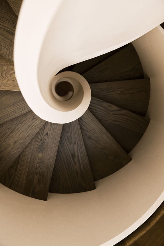 Spiral wooden staircase, viewed from above, showcasing elegant curves and a smooth, white banister.