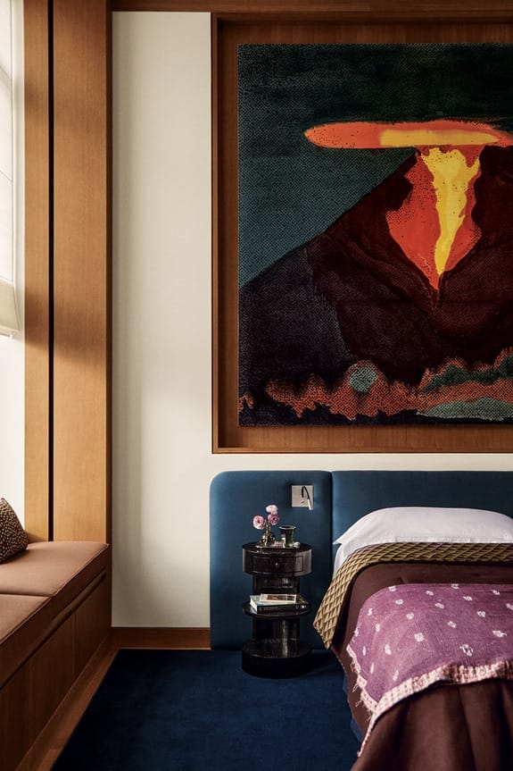 Cozy bedroom with large abstract painting above bed, includes a bench, nightstand, and vibrant decor.