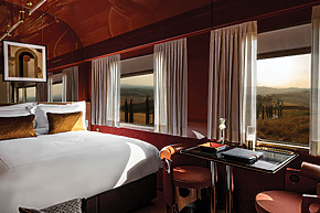 Luxurious train cabin interior with a comfortable bed, elegant decor, and large windows offering scenic countryside views