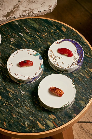 Three plates of sushi on a round marble table, featuring colorful, artistic designs and vibrant sushi pieces.