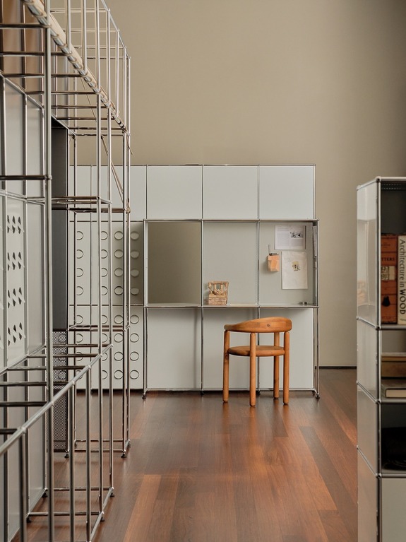 Modern home office with sleek metal shelving, wooden chair, and minimalist white cabinets on a wooden floor.