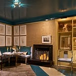 Cozy living room with a fireplace, blue ceiling, art on the walls, and elegant seating near a warmly lit fire.