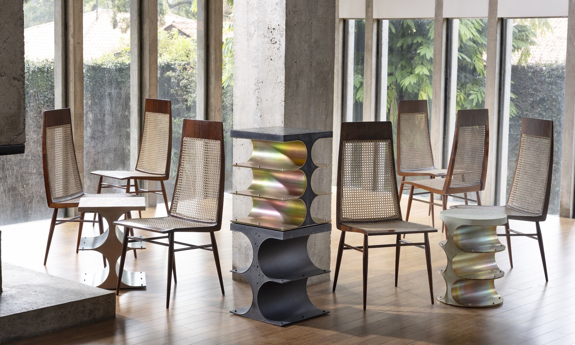 Modern chairs with woven backs and unique metal side tables in a bright room with large windows.