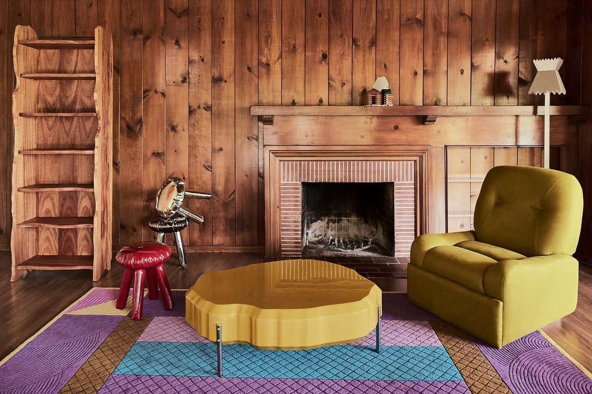 Cozy living room with wood paneling, yellow chair, unique coffee table, red stool, and decorative fireplace.