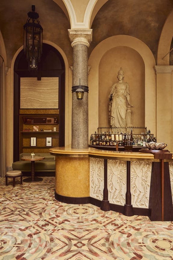 Elegant bar area with a statue, ornate patterns, arched ceiling, and warm lighting in a stylish, classical setting.