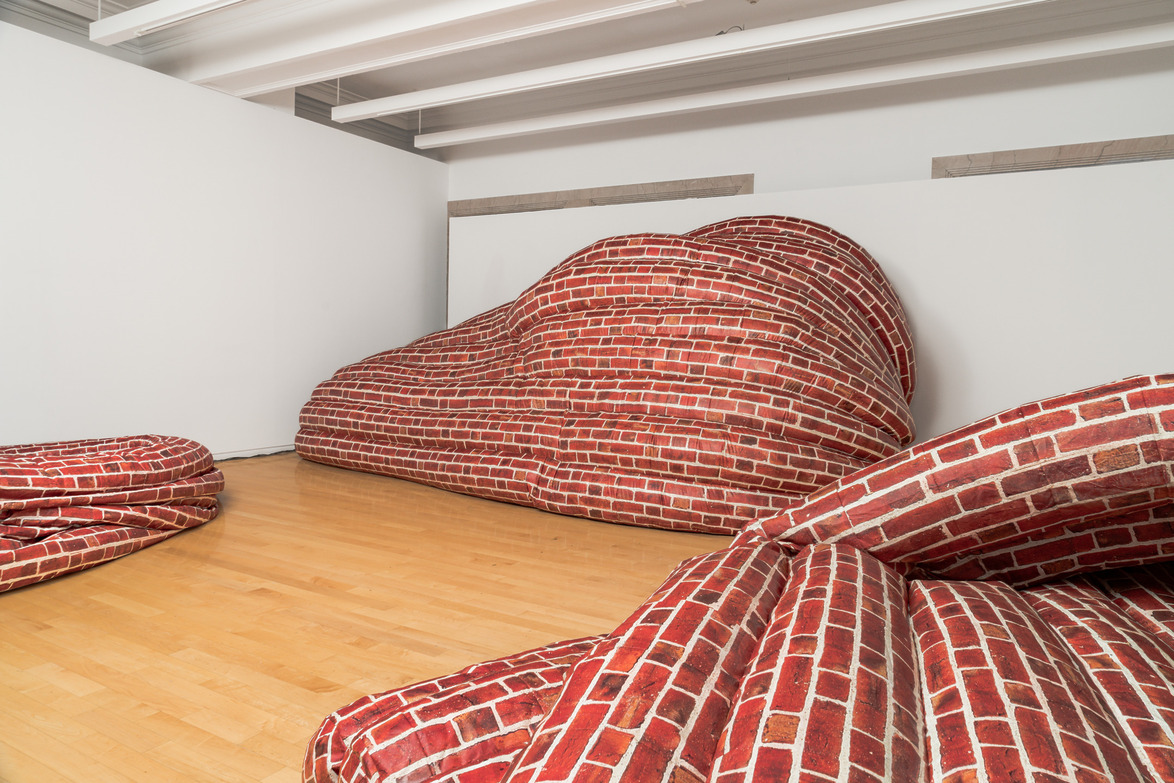 Contemporary art installation with fabric resembling red brick walls, draped across a gallery floor and against white walls.