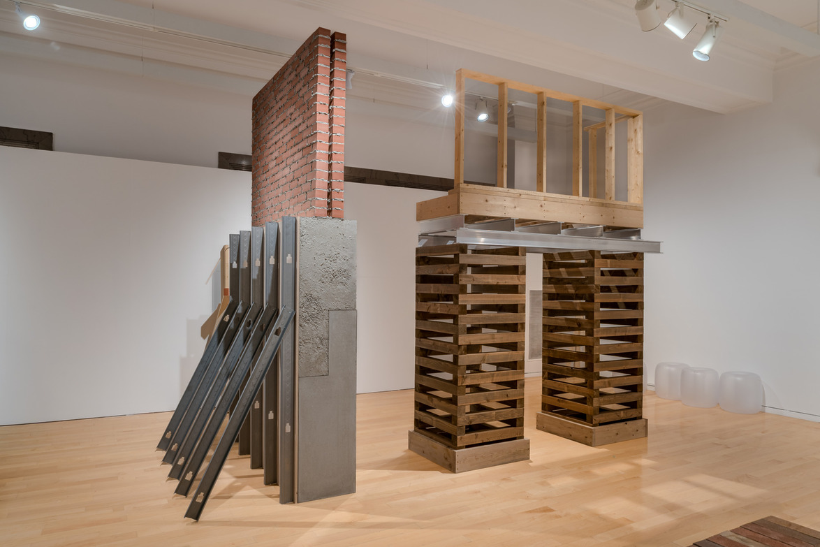 Modern art installation with wooden, metal, and brick elements in a gallery setting on a polished wooden floor.