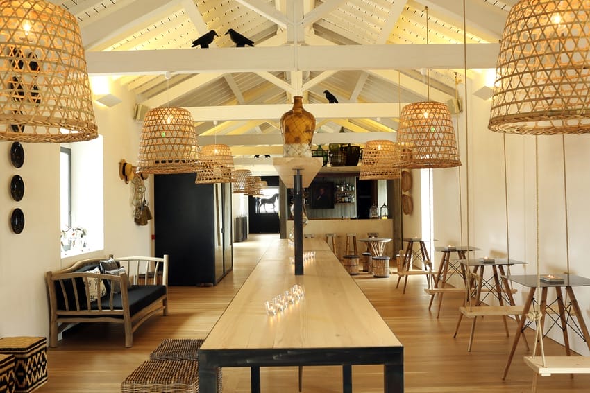 Spacious modern dining area with wooden beams, wicker lamps, long table, and cozy seating.