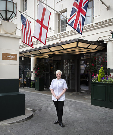 Chef standing outside a building with three flags displayed above the entrance, including the American and British flags.