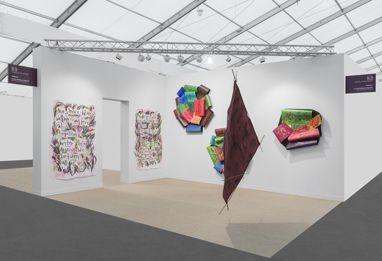 Art exhibit with colorful abstract paintings and sculptures displayed on white walls under a well-lit tented space.