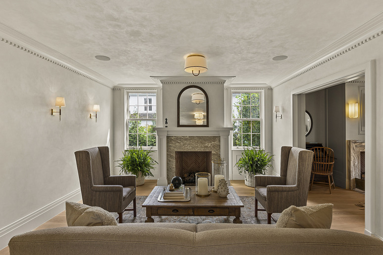Elegant living room with fireplace, two armchairs, sofa, coffee table, lush green plants, and soft lighting fixtures.