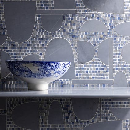 Blue and white ceramic bowl on a shelf with a geometric patterned gray and blue mosaic tile background.