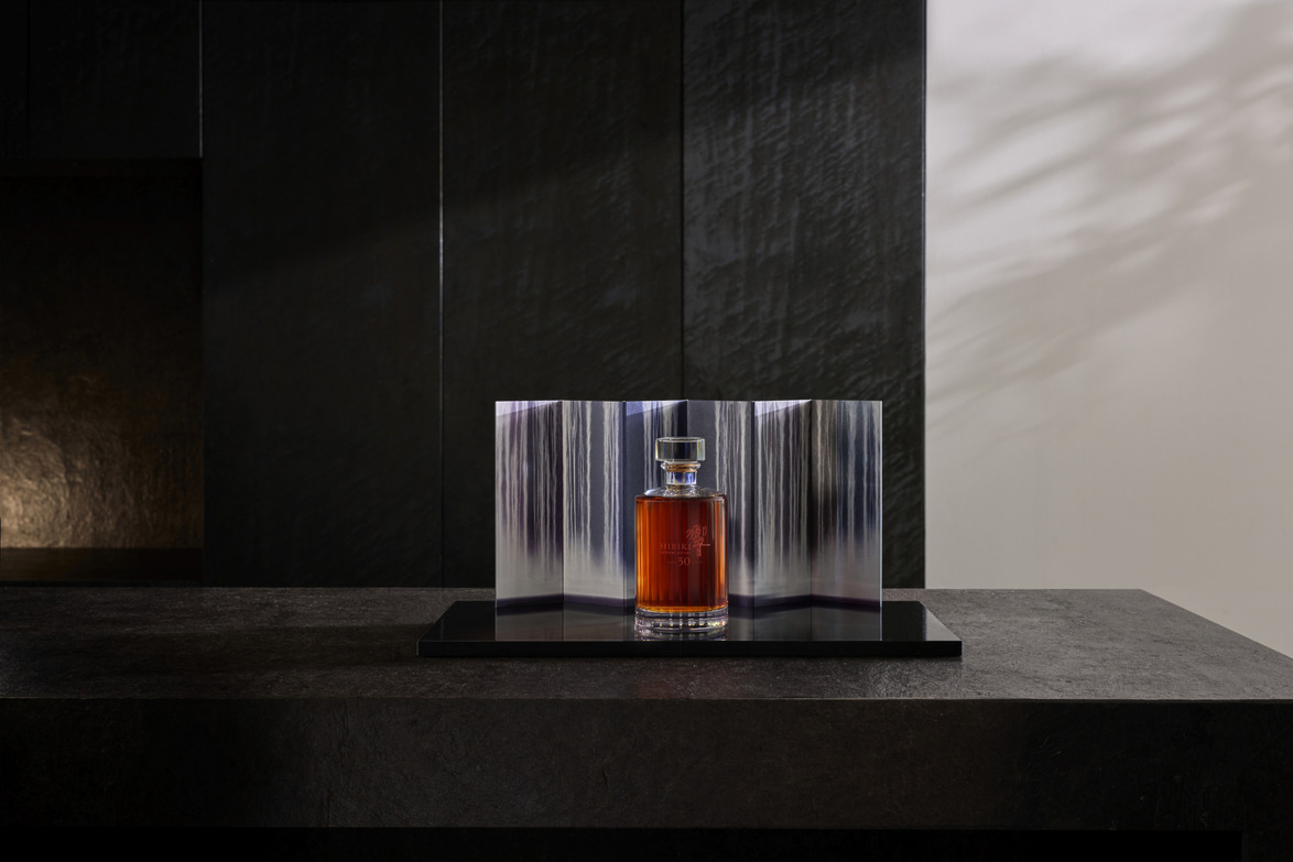 Elegant perfume bottle displayed on a dark, sleek surface with artistic background shadows and lighting.