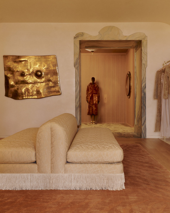 Luxurious boutique interior with elegant sofa, gold wall art, and clothing in a well-lit room.