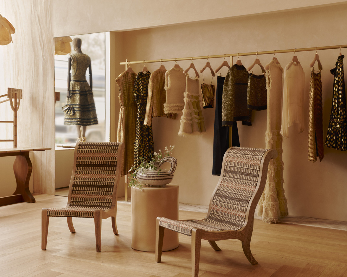 Elegant boutique interior with woven chairs, a round table, and clothing displayed on a rack, featuring stylish dresses.