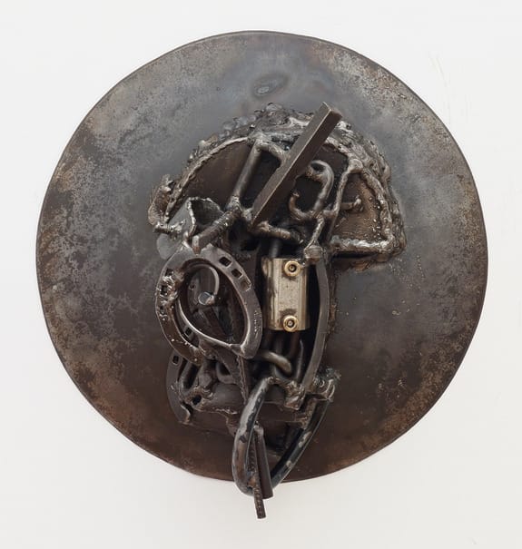 Abstract metal sculpture with circular base featuring welded horseshoes and various metal elements.